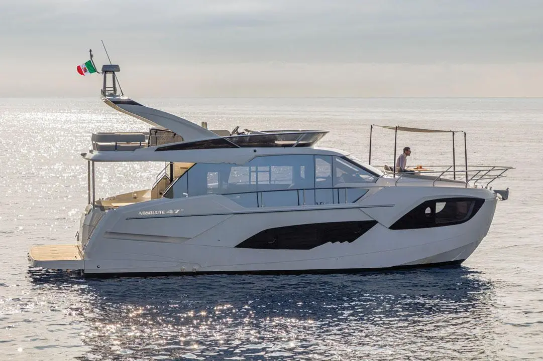 A sleek white yacht, "Absolute 47," floats on calm waters, with a man dining on the deck under a sunshade.
